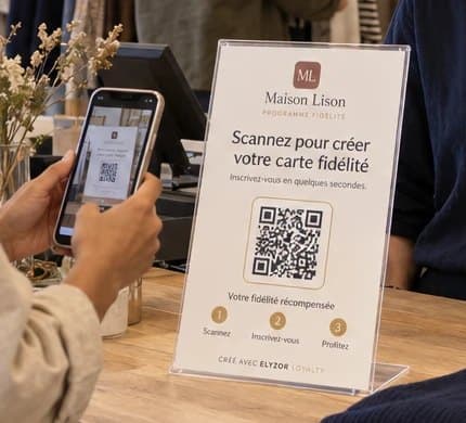 Support QR du programme de fidélité posé sur le comptoir d’une boutique de vêtements, scanné par une cliente