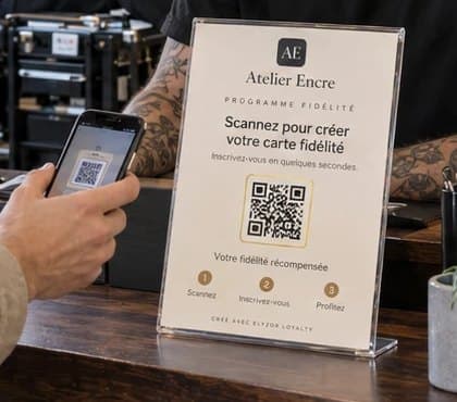 Support QR du programme de fidélité posé sur le comptoir d’un studio de tatouage, scanné par un client